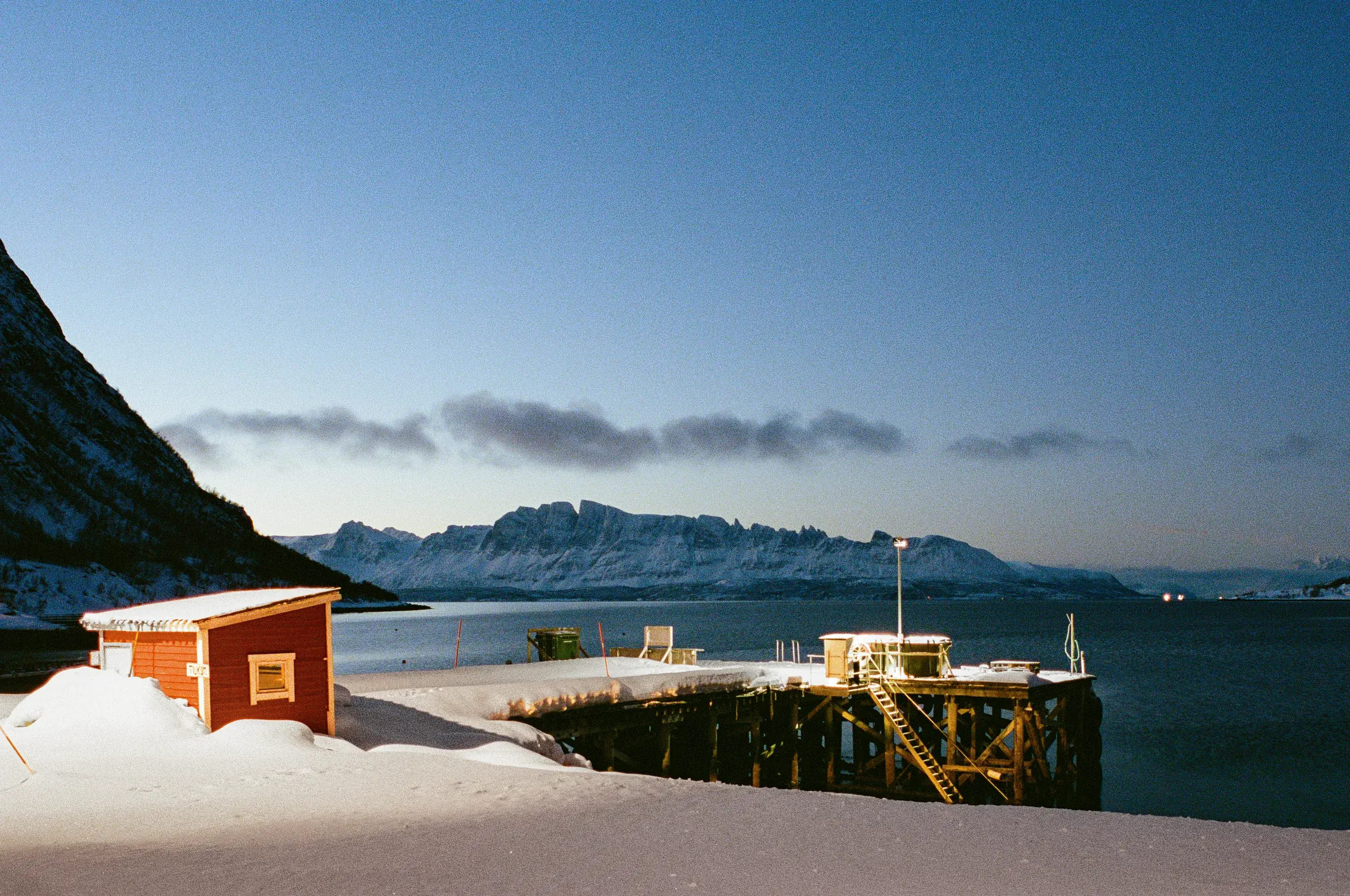A red cabin on a snowy fjord shore at blue hour, metered through Second View